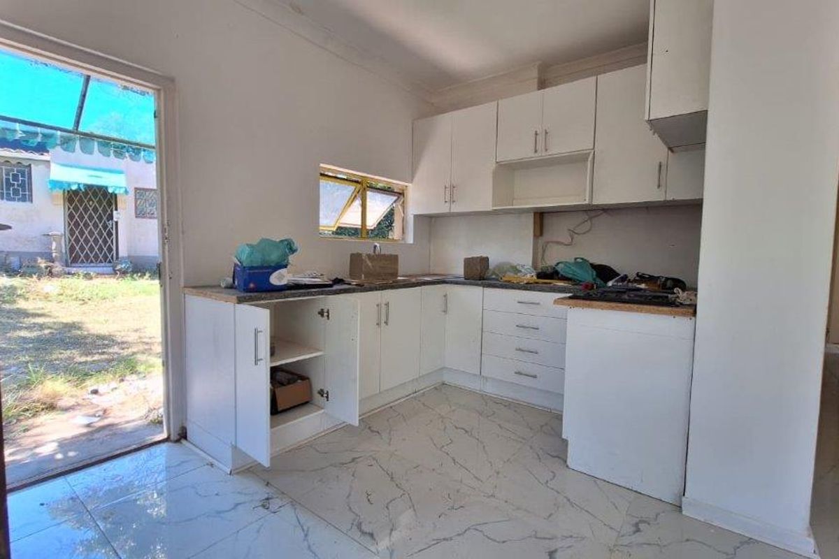 A compact kitchen featuring white cabinetry, marble-look floor tiles, and direct access to the rear garden area, currently requiring finishing touches.