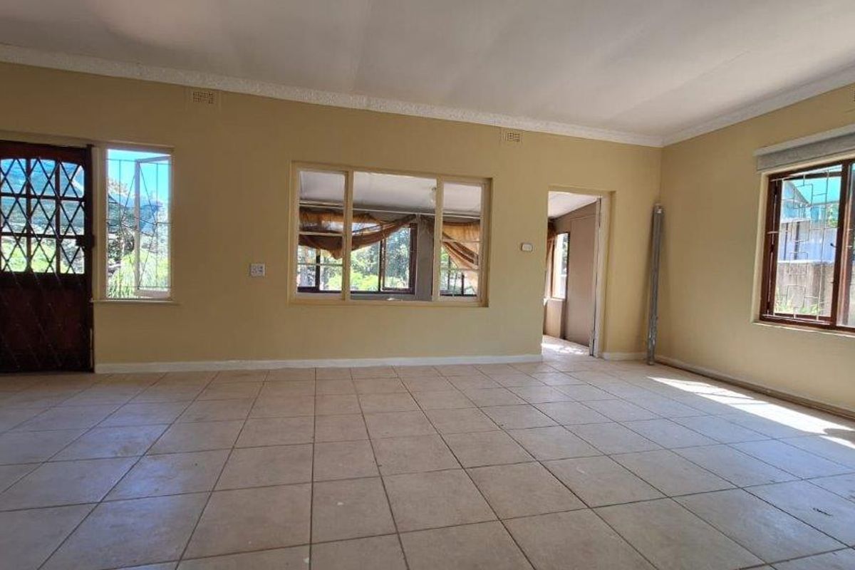 A spacious, empty living area featuring tiled flooring, large windows for natural light, and a secure entrance door.