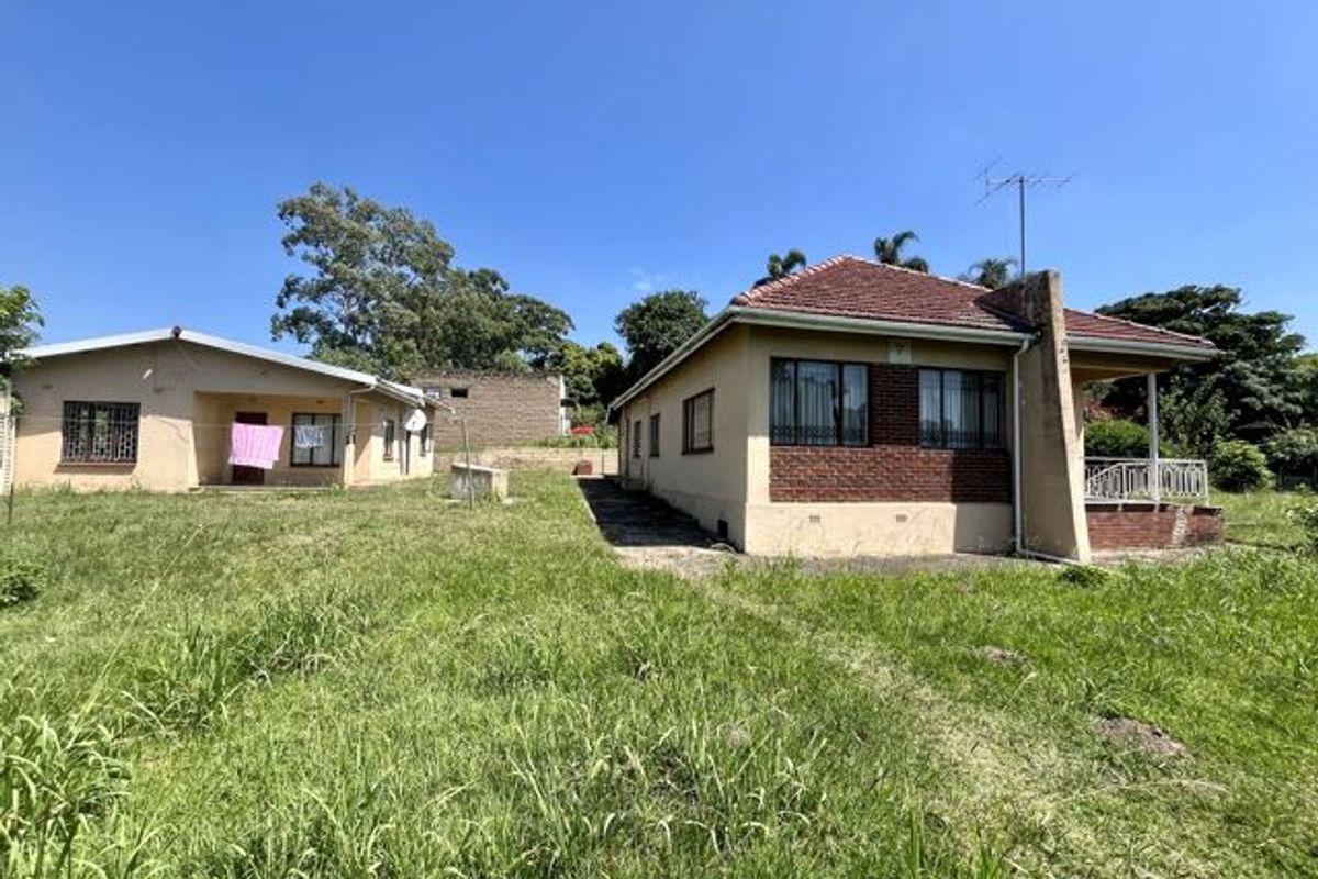Rear view of the property showing two detached structures with tiled roofs, brick accents, and security bars on windows, set on a large grassed plot.