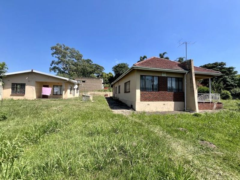 Rear view of the property showing two detached structures with tiled roofs, brick accents, and security bars on windows, set on a large grassed plot.