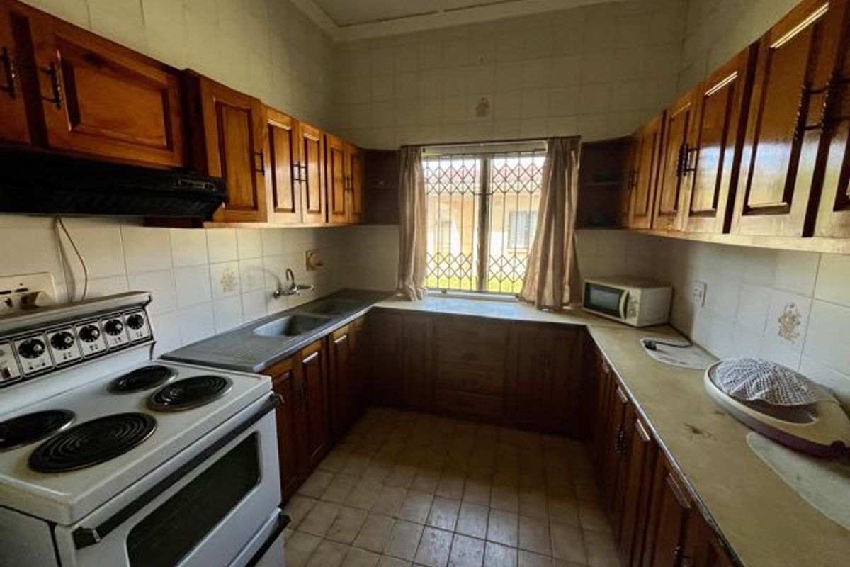 A dated kitchen featuring wooden cabinetry, tiled splashbacks, and a functional electric stove with an integrated extractor fan.