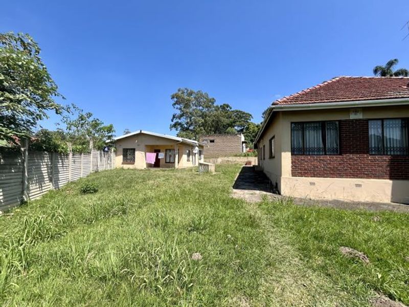 Rear view of the property showing a large grassed yard, concrete pathways, and the exterior brick and plaster facade of the main house and outbuilding.