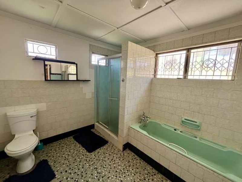 A dated bathroom featuring a green bathtub, separate shower enclosure, and tiled finishes. The space is vacant and ready for renovation.