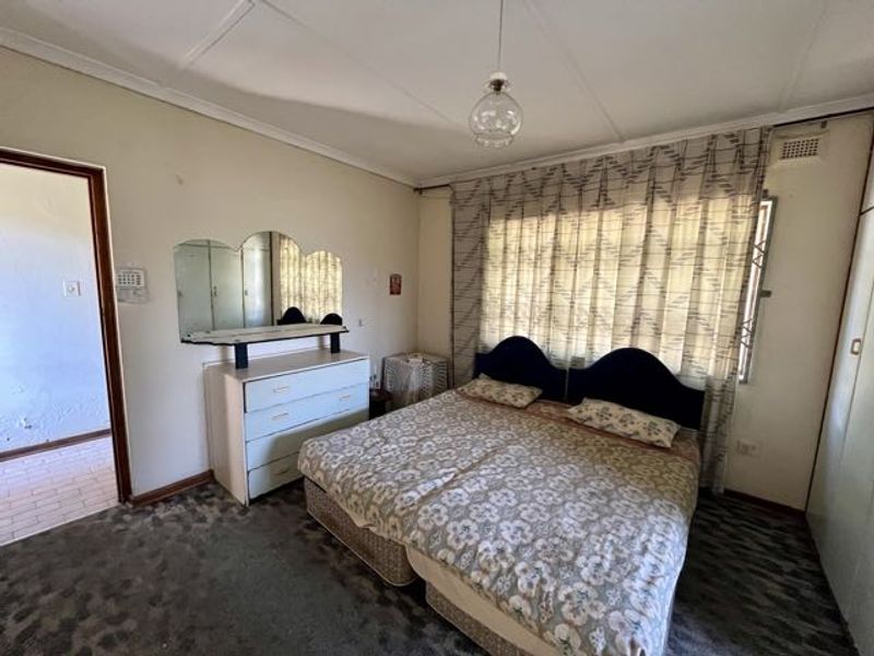 A spacious bedroom featuring built-in cupboards, carpeted flooring, and large windows with curtains, offering a functional layout ready for modernization.