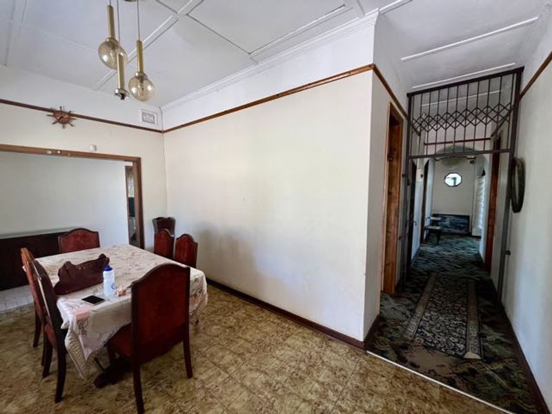 Dining area featuring decorative ceiling panels and tiled flooring, leading into a hallway secured by a metal gate.