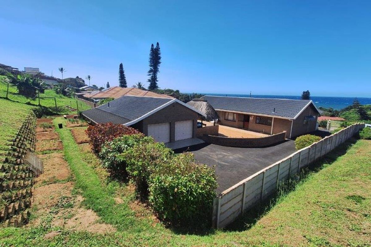 Aerial view of a residential property featuring a double garage, paved driveway, and expansive grounds with coastal views.