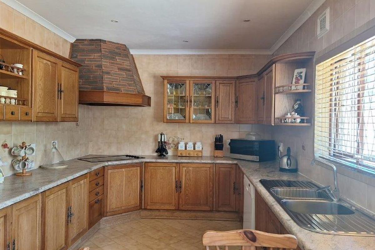 A traditional kitchen featuring solid wood cabinetry, a brick-style extractor hood, laminate countertops, and a double stainless steel sink with tiled splashbacks.