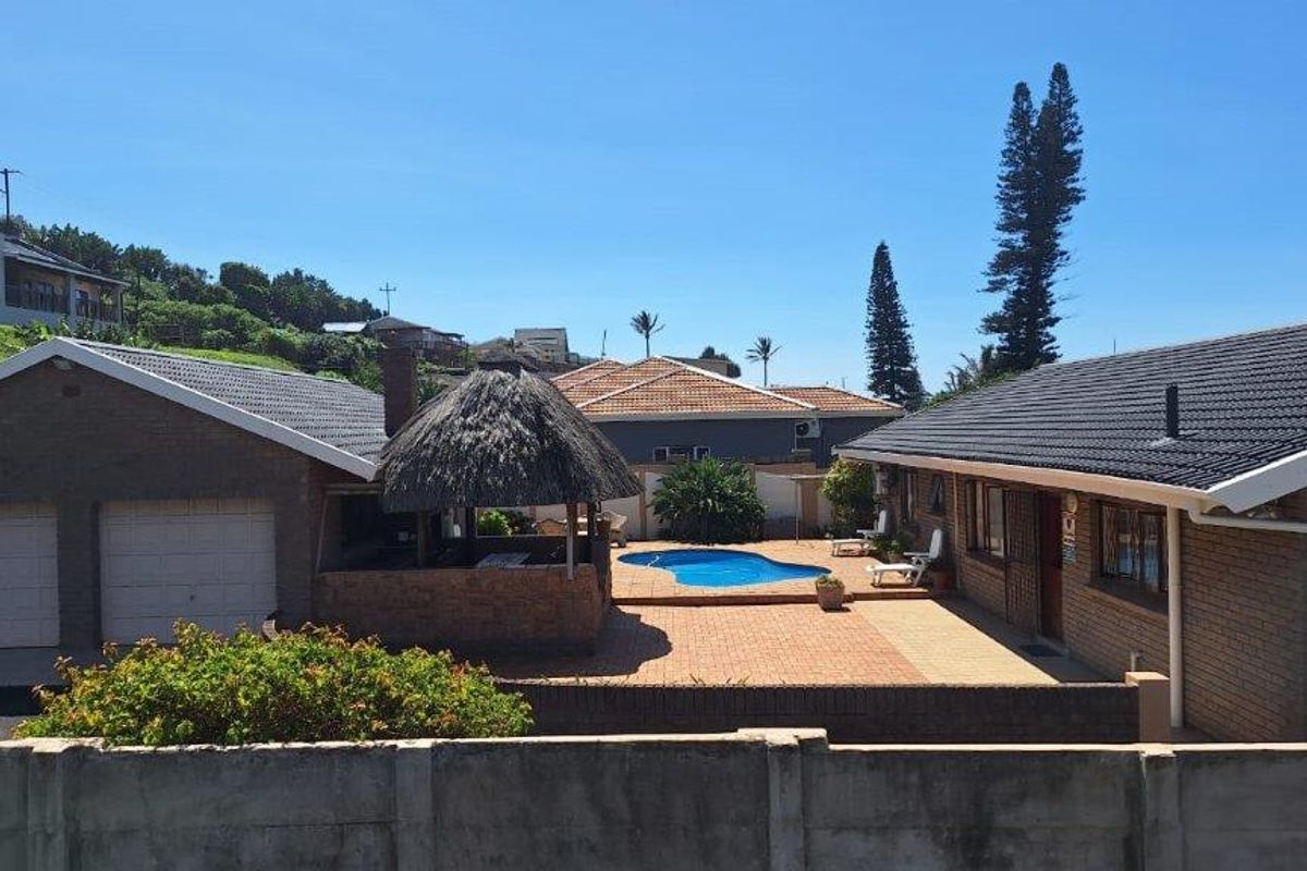 Rear exterior view featuring a swimming pool, a traditional thatched lapa, brick paving, and a double garage set within a private garden area.