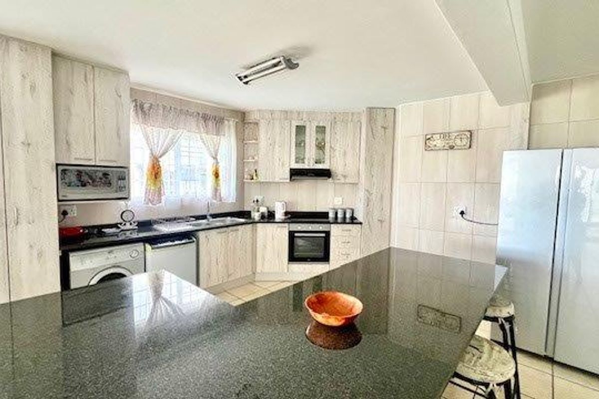A functional kitchen featuring light wood-grain cabinetry, granite countertops, a breakfast bar, and integrated appliances with tiled finishes throughout.