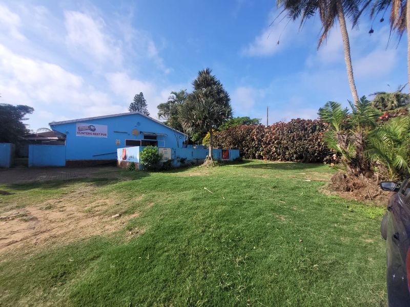 Exterior view of a commercial property featuring a blue facade, paved driveway, and surrounding garden area.