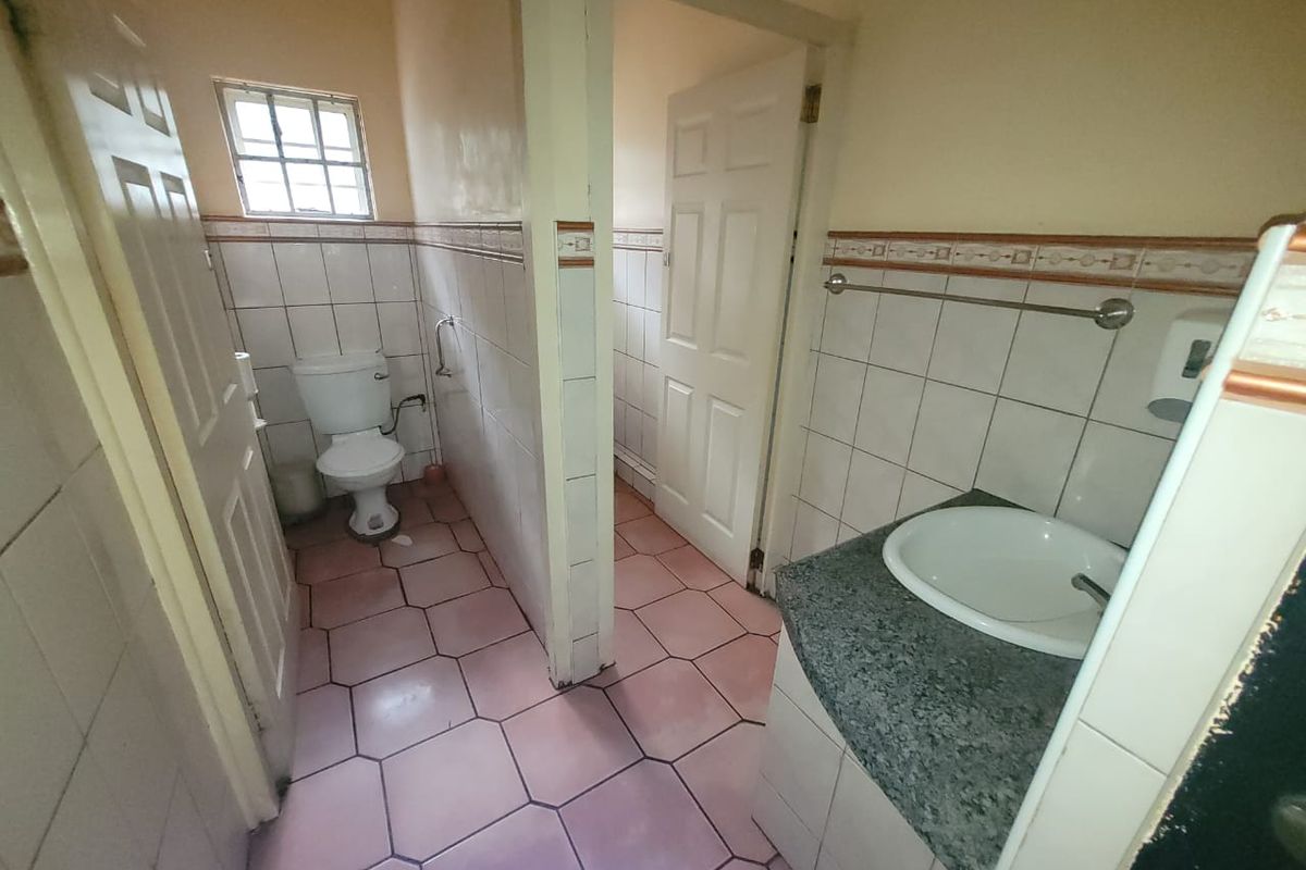 A functional commercial bathroom featuring a built-in vanity with a ceramic basin, tiled walls, and ceramic floor tiles.
