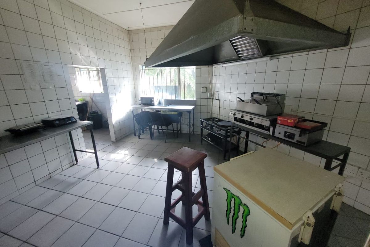Commercial kitchen area featuring tiled surfaces, stainless steel prep stations, and a large overhead extractor hood, suitable for food preparation and service.