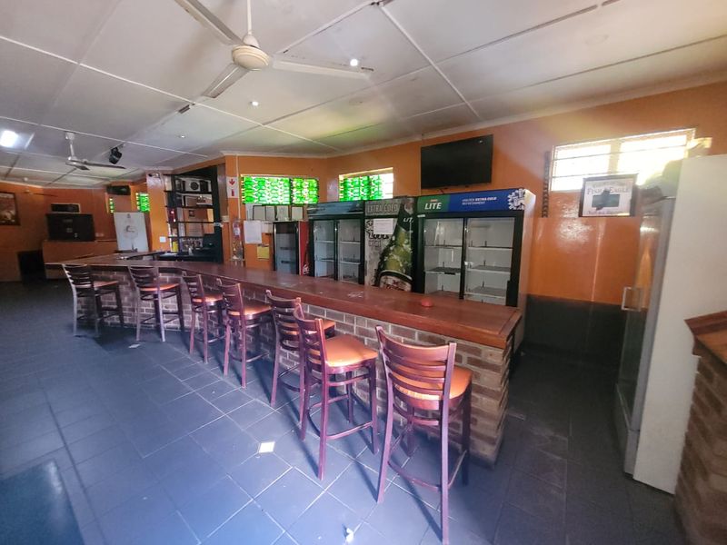 A commercial bar area featuring a brick-based counter, tiled flooring, ceiling fans, and integrated commercial display refrigeration units.