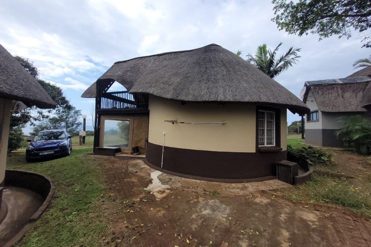 Rear view of a circular townhouse featuring a traditional thatch roof, brick paved surrounds, and an upper-level balcony area.