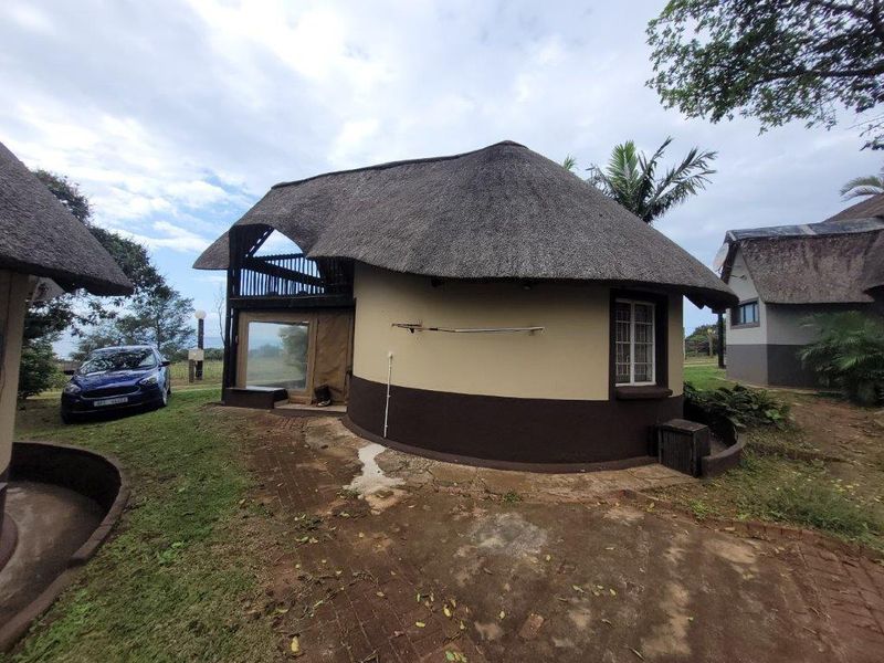 Rear view of a circular townhouse featuring a traditional thatch roof, brick paved surrounds, and an upper-level balcony area.