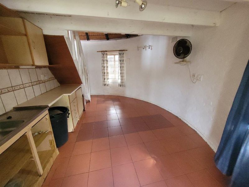 An open-plan living and kitchen area featuring tiled flooring, exposed ceiling beams, and basic built-in cabinetry in a dated condition.