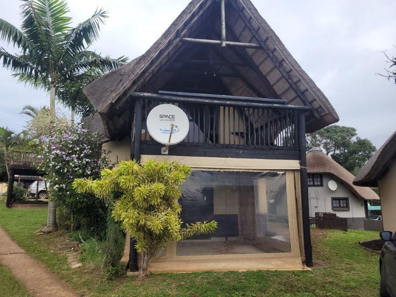 Front view of a two-story townhouse featuring a traditional thatched roof, a timber balcony, and a ground-level patio enclosed with clear PVC screens.