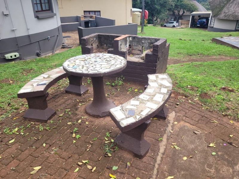 Rear exterior area featuring a paved patio, built-in brick braai, and integrated concrete seating, set within a garden space.