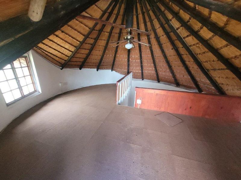 An attic-style bedroom featuring a traditional thatched roof with exposed timber rafters, a ceiling fan, and a timber staircase balustrade.