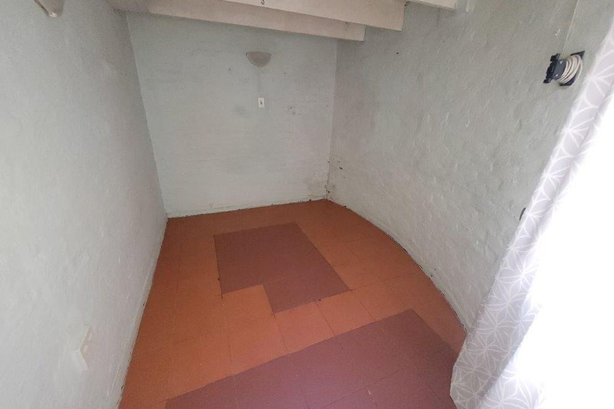 A small, empty room featuring exposed ceiling beams and tiled flooring, requiring cosmetic updates and finishing touches to improve its overall condition and appeal.