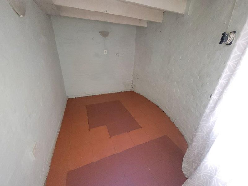 A small, empty room featuring exposed ceiling beams and tiled flooring, requiring cosmetic updates and finishing touches to improve its overall condition and appeal.