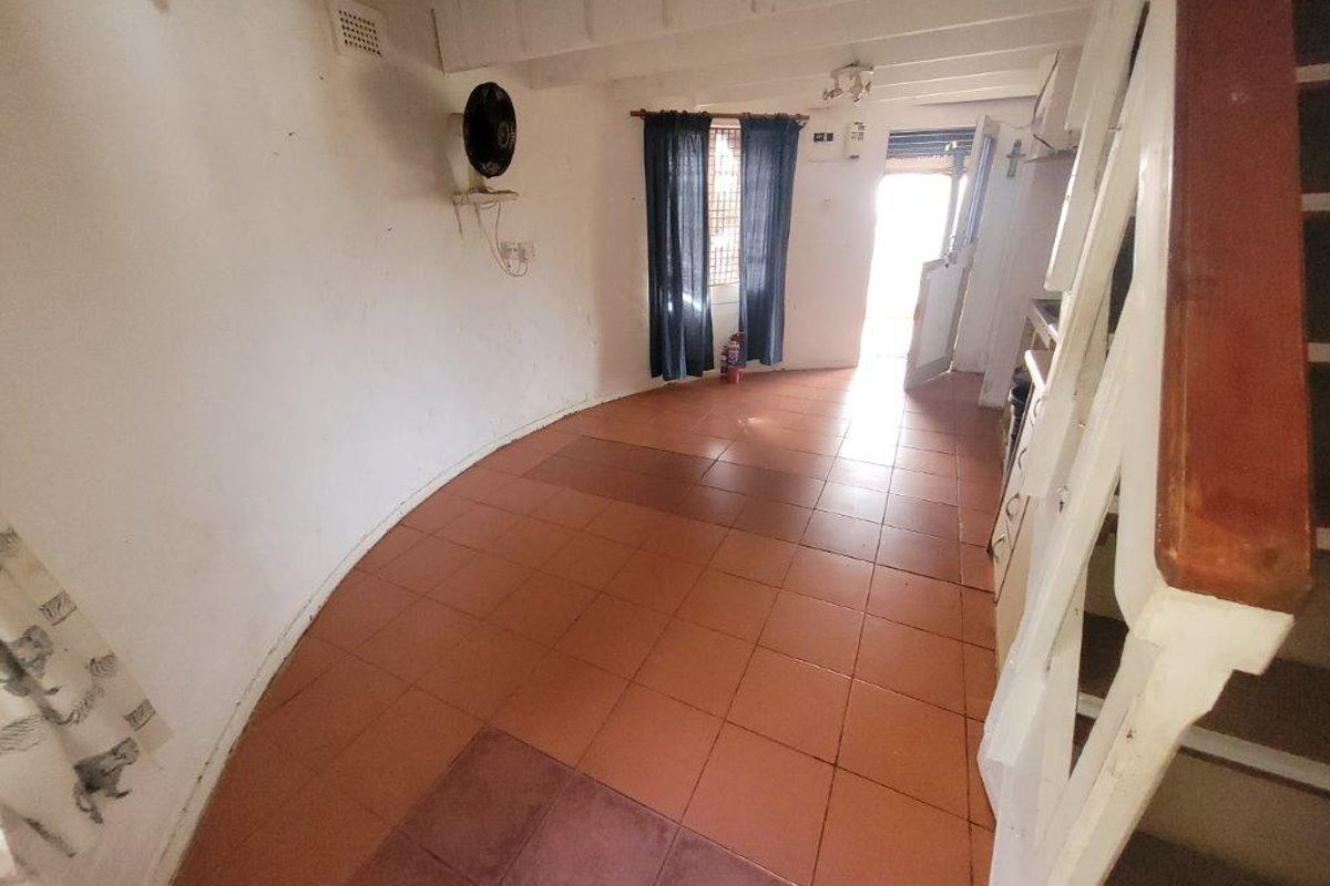 An empty living area featuring tiled flooring, exposed ceiling beams, and a staircase, offering a blank canvas for renovation and interior design updates.