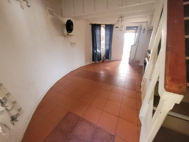 An empty living area featuring tiled flooring, exposed ceiling beams, and a staircase, offering a blank canvas for renovation and interior design updates.