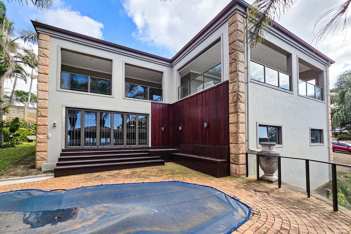 Rear exterior view featuring a paved patio area, swimming pool with cover, stone and timber facade detailing, and upper-level balconies.