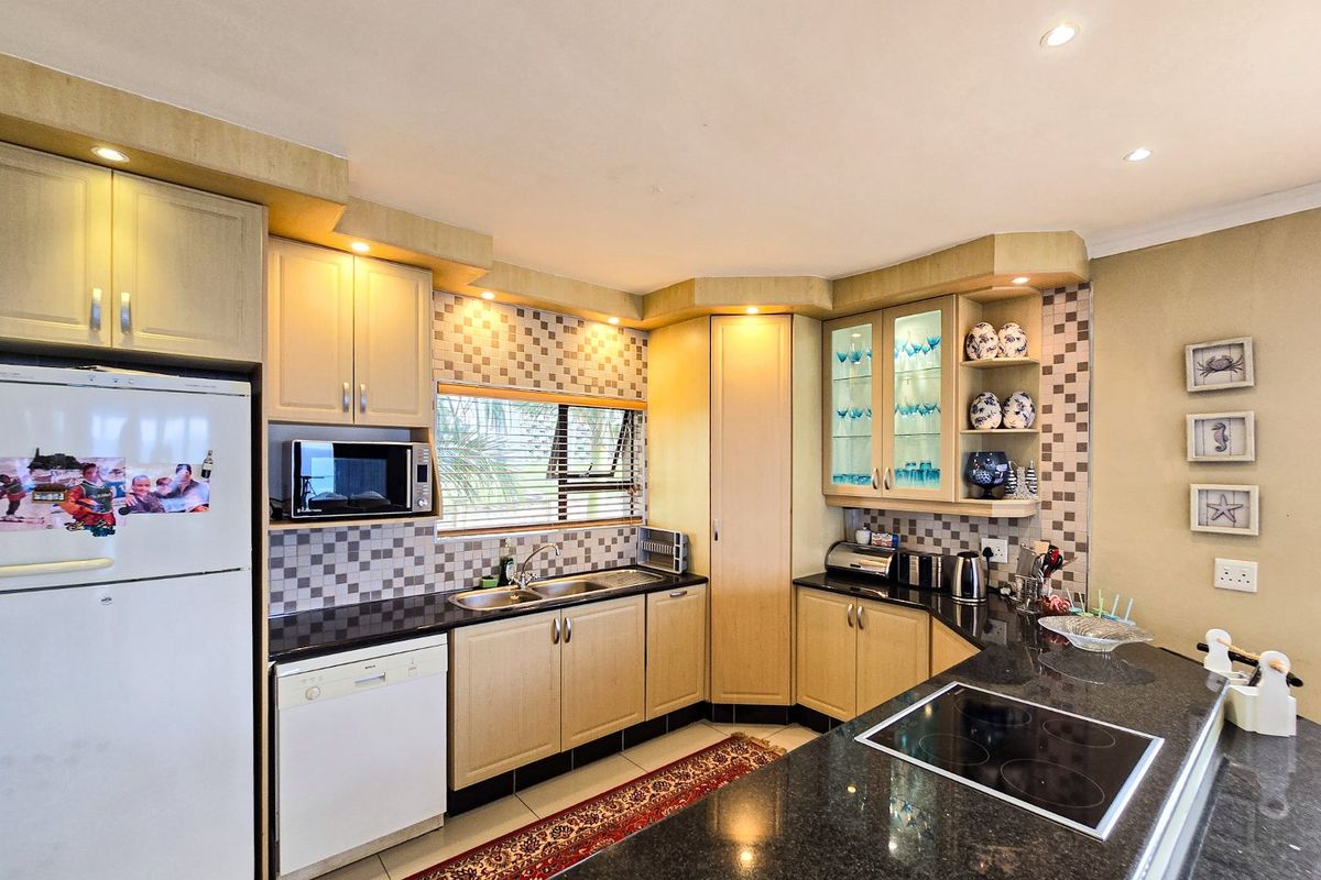 A functional kitchen featuring light wood cabinetry, dark granite countertops, a built-in hob, and a tiled backsplash with integrated lighting.
