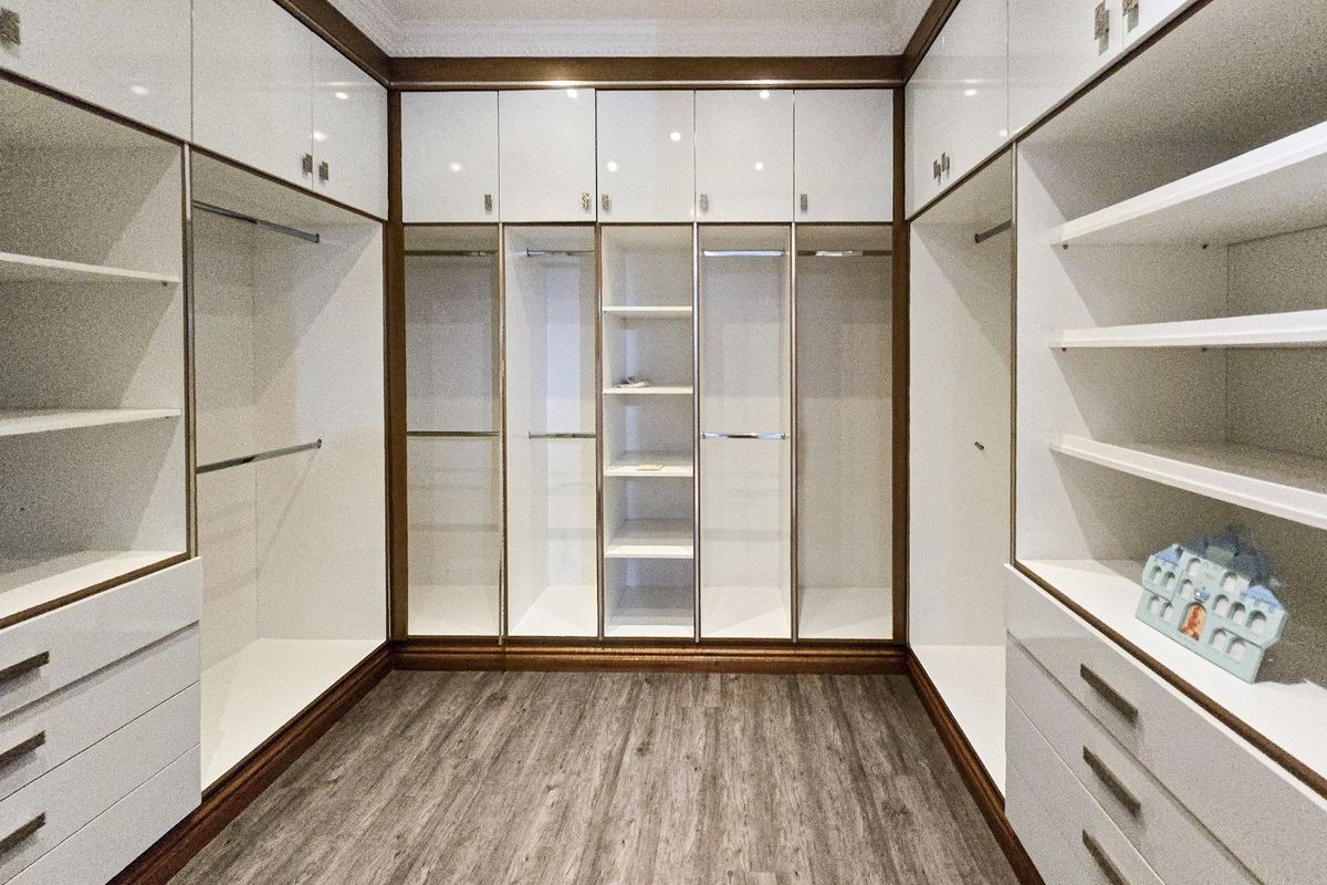 A spacious walk-in closet featuring extensive custom built-in cabinetry with high-gloss white finishes, integrated shelving, hanging rails, and drawers.