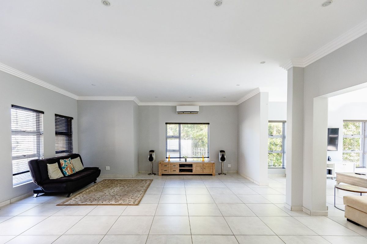 Spacious living area featuring neutral tiled flooring, crown molding, recessed lighting, and a wall-mounted air conditioning unit with large windows.