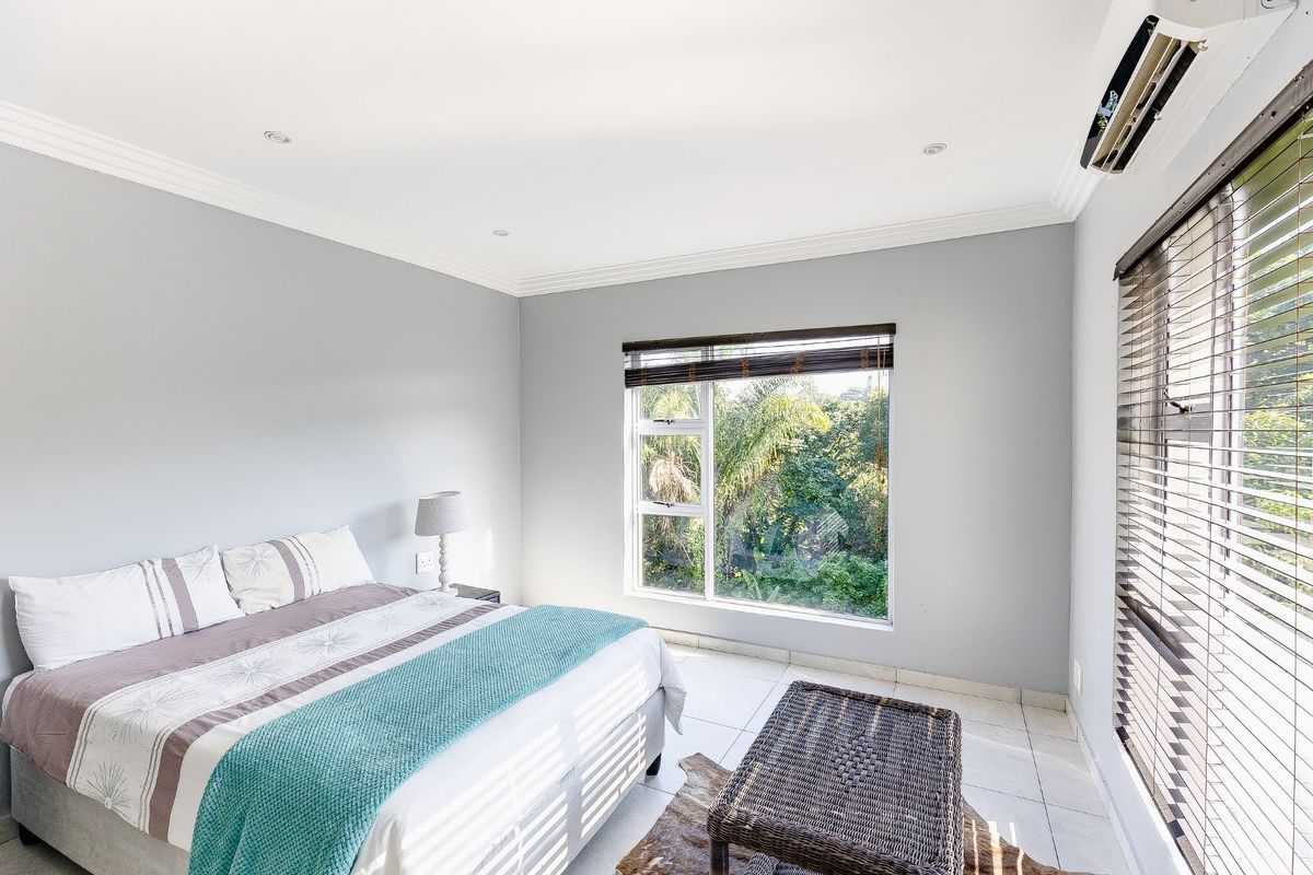 A bright and well-maintained bedroom featuring tiled flooring, recessed lighting, a split-system air conditioner, and large windows with garden views.