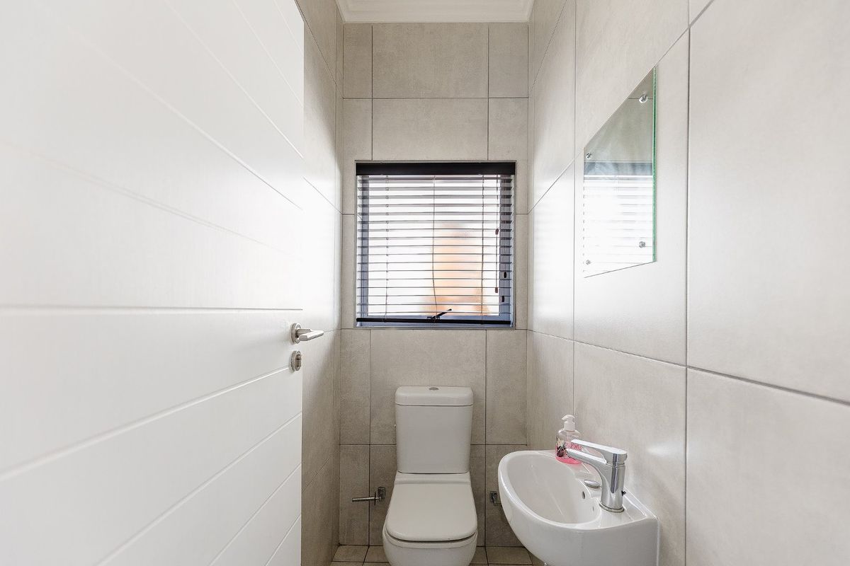 A clean and modern guest cloakroom featuring neutral wall tiles, a wall-mounted basin, and a toilet.
