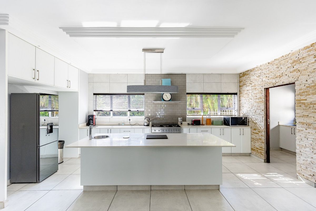 Modern kitchen featuring a central island, stone cladding feature wall, gas cooktop, extractor fan, and ample built-in cabinetry with tiled flooring.