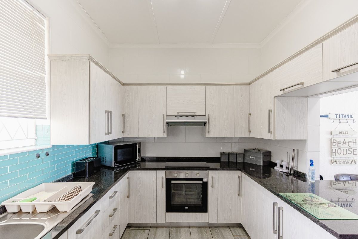 A functional kitchen featuring light wood-grain cabinetry, dark granite countertops, a built-in oven and hob, and a vibrant blue tiled backsplash.