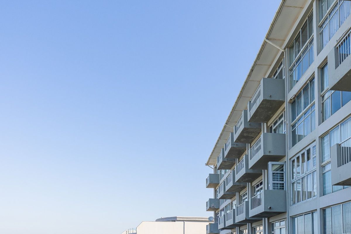 Exterior view of an apartment building facade featuring multiple stacked balconies with metal railings and large sliding glass doors.