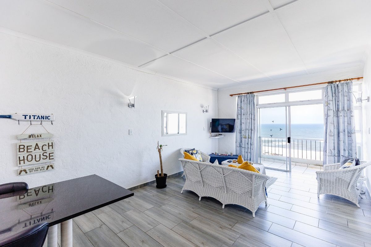 Bright open-plan living area featuring tiled flooring, wall sconces, and direct access to a balcony with ocean views.