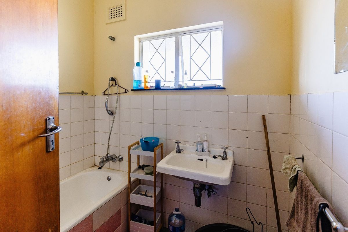 A dated bathroom featuring a wall-mounted basin, bathtub with shower mixer, and tiled walls, requiring modernization to improve its overall condition and appeal.