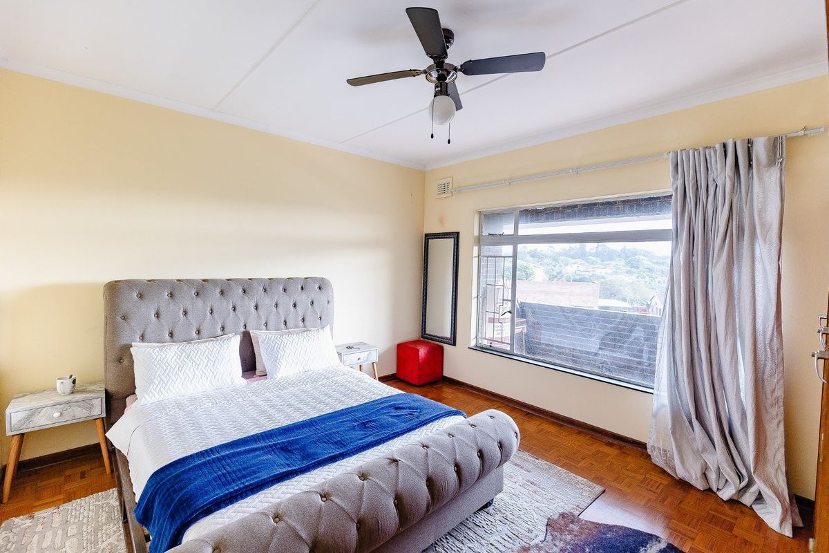A well-lit bedroom featuring classic parquet flooring, a ceiling fan, and a large window that provides natural light and exterior views.