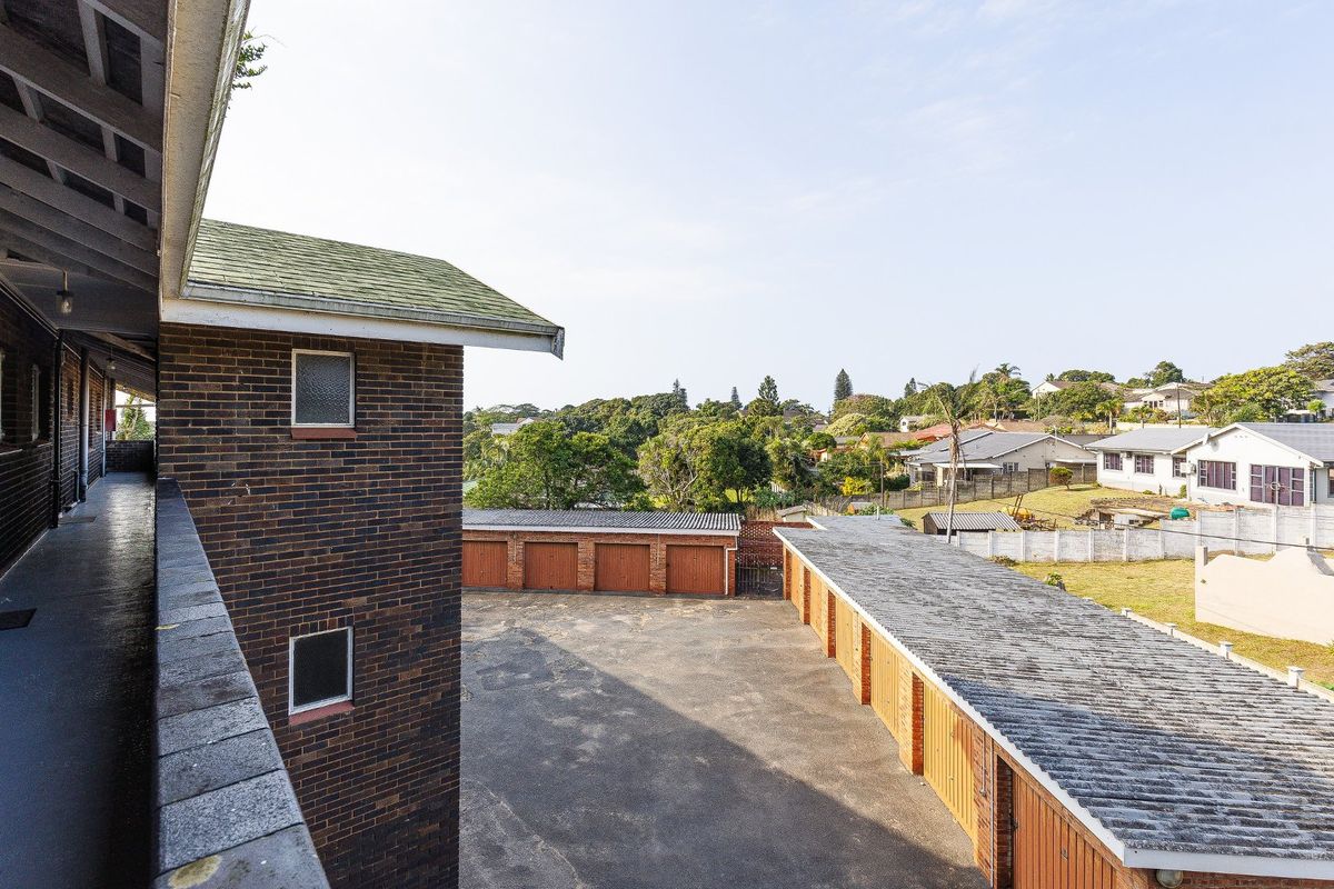An elevated view of the apartment complex exterior, featuring a brick facade, balcony walkway, and a shared parking area with multiple garage units.
