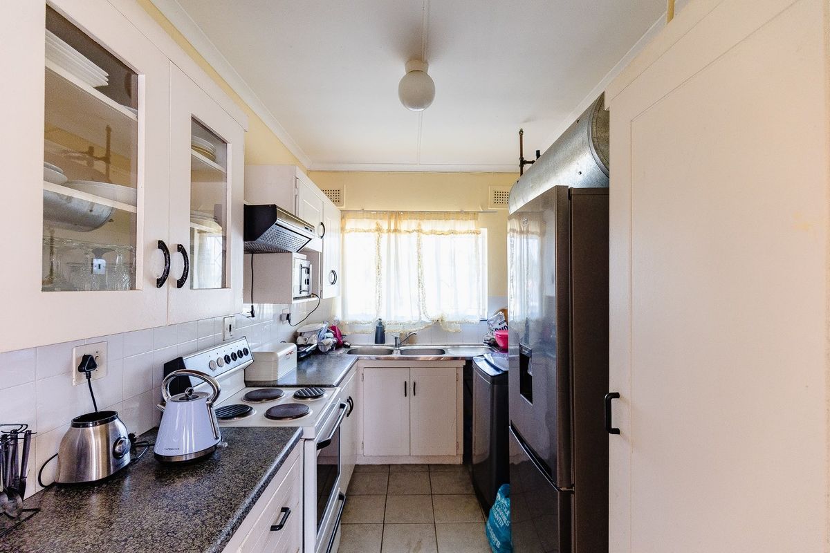 A functional galley-style kitchen featuring built-in cabinetry, laminate countertops, a stainless steel sink, and an electric stove with an extractor fan.
