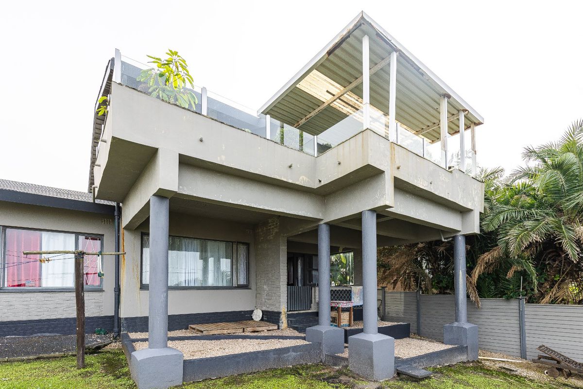 Rear view of the property featuring a covered ground-floor patio and an elevated balcony with glass balustrades and metal roofing.