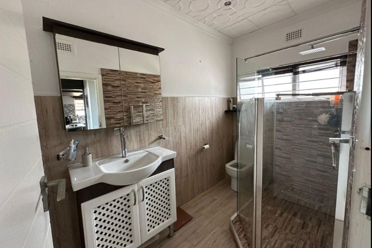 Modern bathroom featuring a vanity with basin, glass-enclosed shower, toilet, and decorative ceiling finishes with wood-look wall and floor tiling.