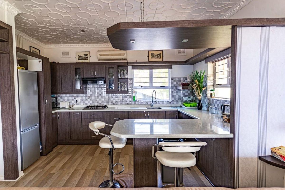 Modern kitchen featuring dark wood cabinetry, stone countertops, a breakfast bar, gas hob, and decorative ceiling tiles.
