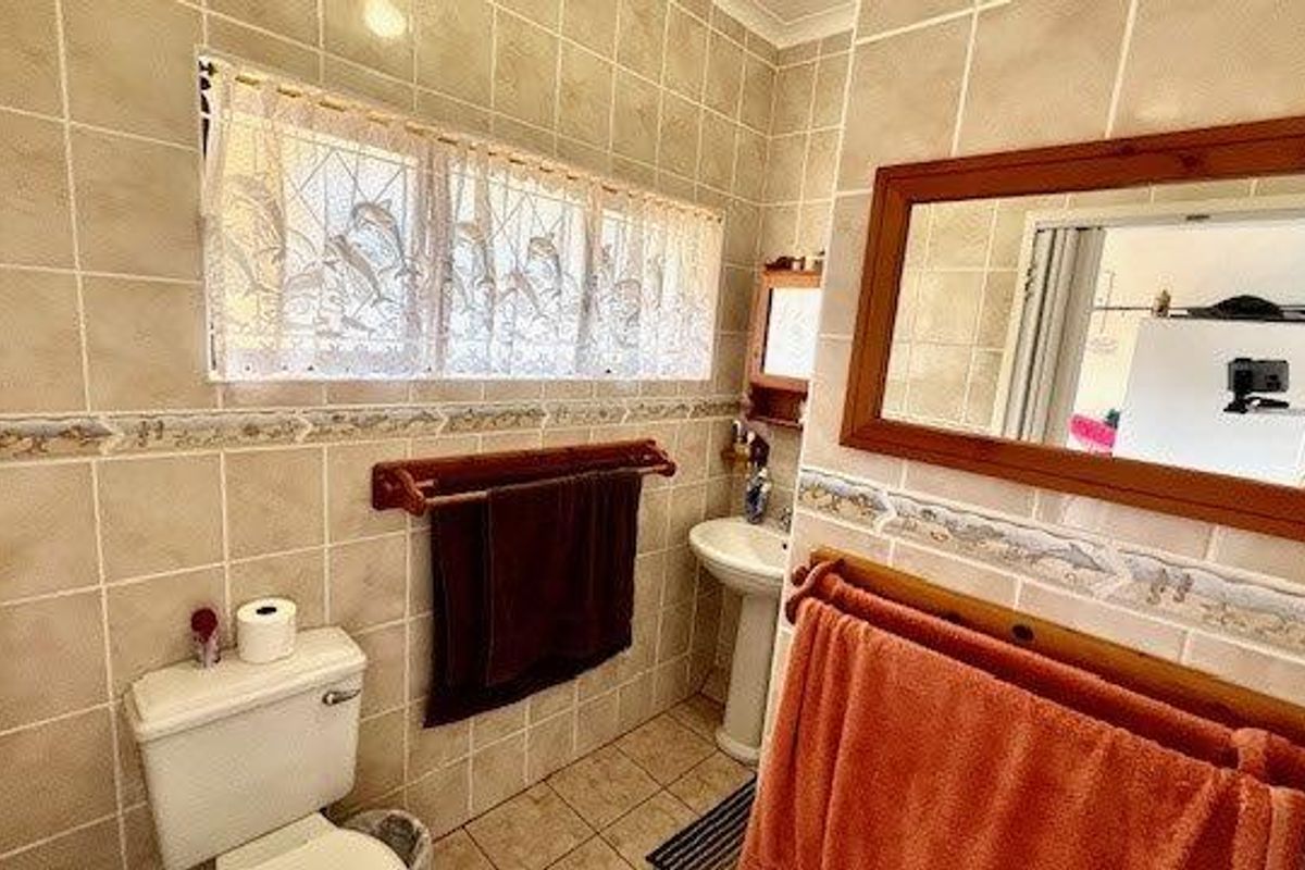 A functional bathroom featuring ceramic wall and floor tiles, a pedestal basin, and a built-in mirror with a wooden frame.