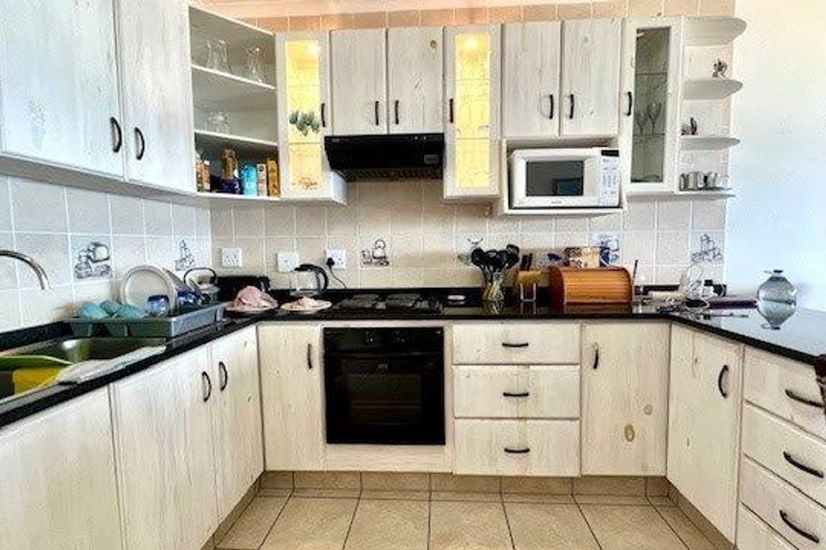 A functional U-shaped kitchen featuring light wood-finish cabinetry, granite countertops, built-in oven, hob, and extractor fan with a tiled backsplash.