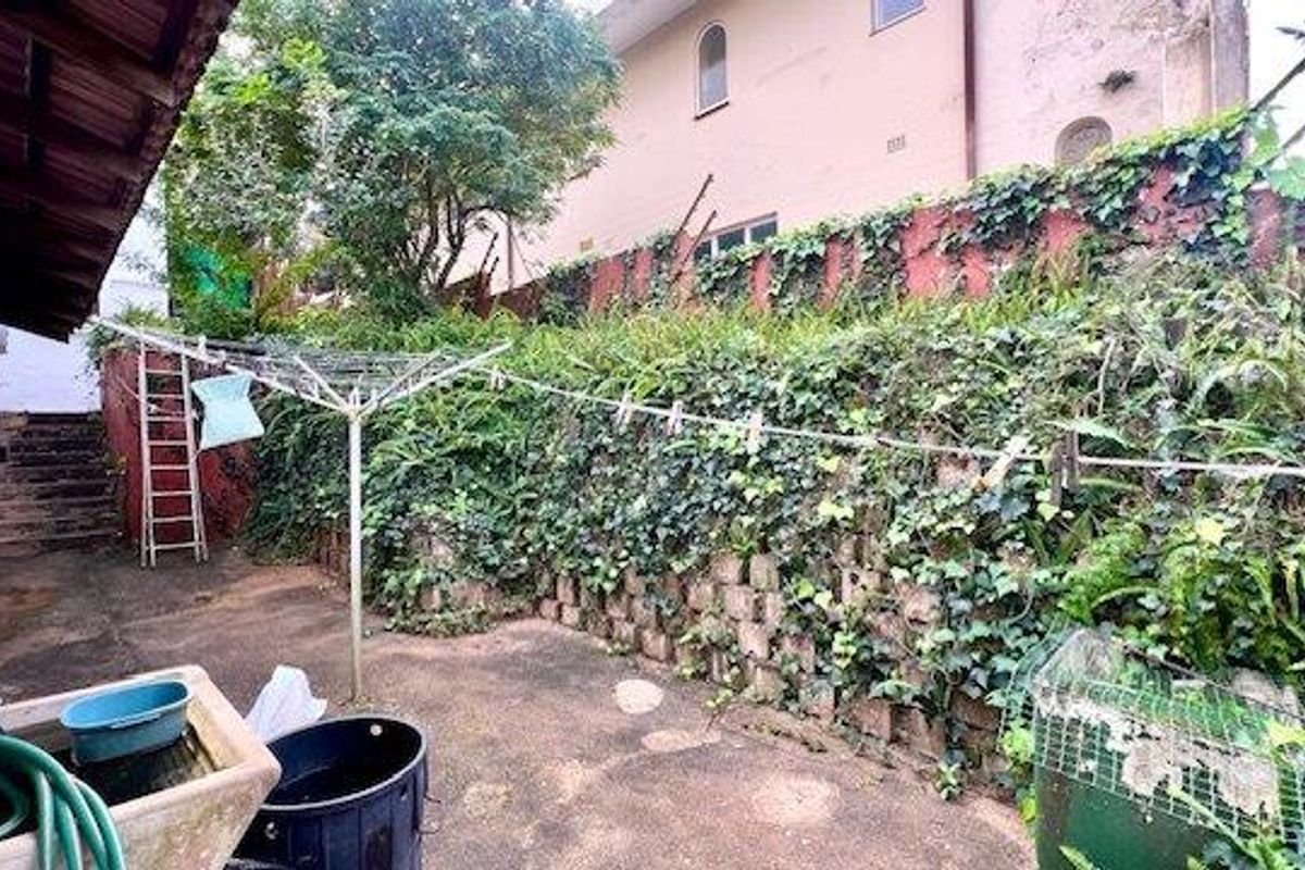 Rear exterior area featuring a concrete paved courtyard, stone basin, and a tiered retaining wall covered in dense ivy.