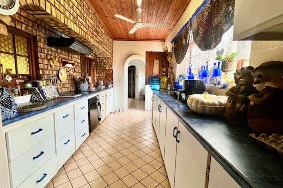 A galley-style kitchen featuring exposed brick walls, timber ceilings, tiled flooring, and extensive built-in cabinetry with a functional layout.