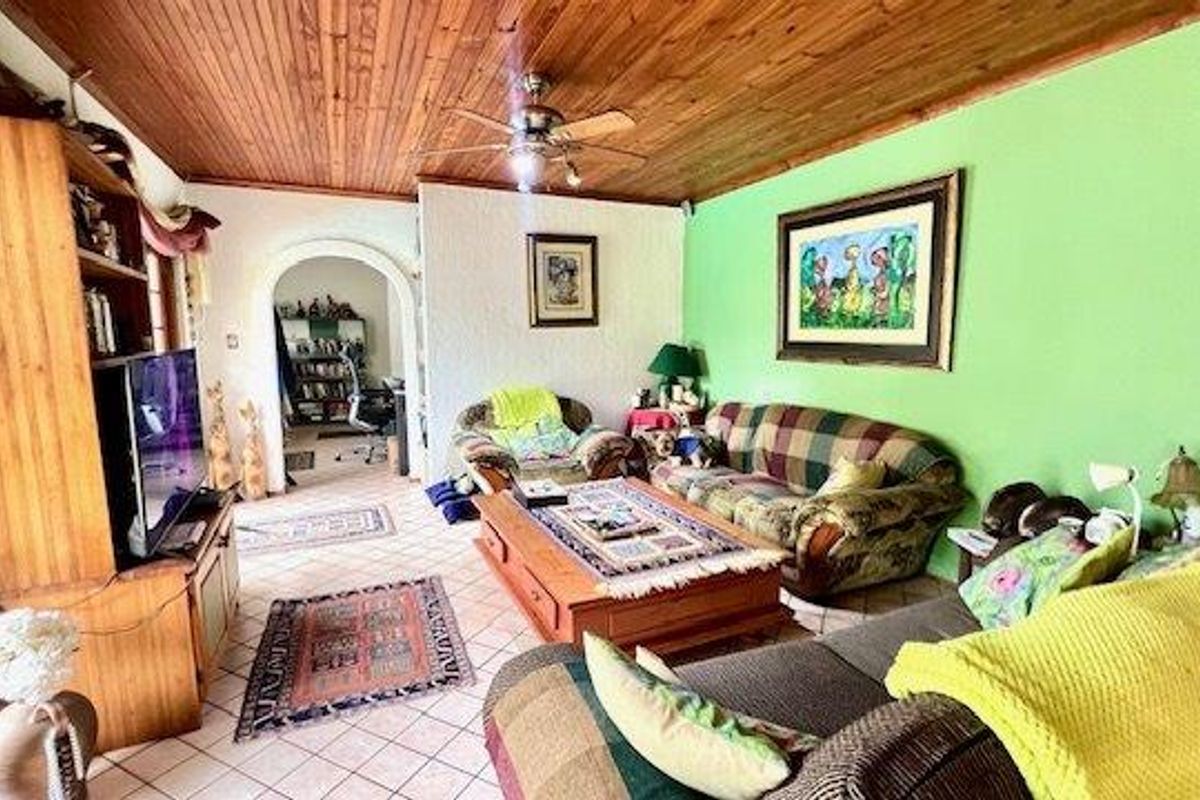 A living room featuring a timber-clad ceiling, ceiling fan, and tiled flooring, connected to an adjacent space through an arched doorway.