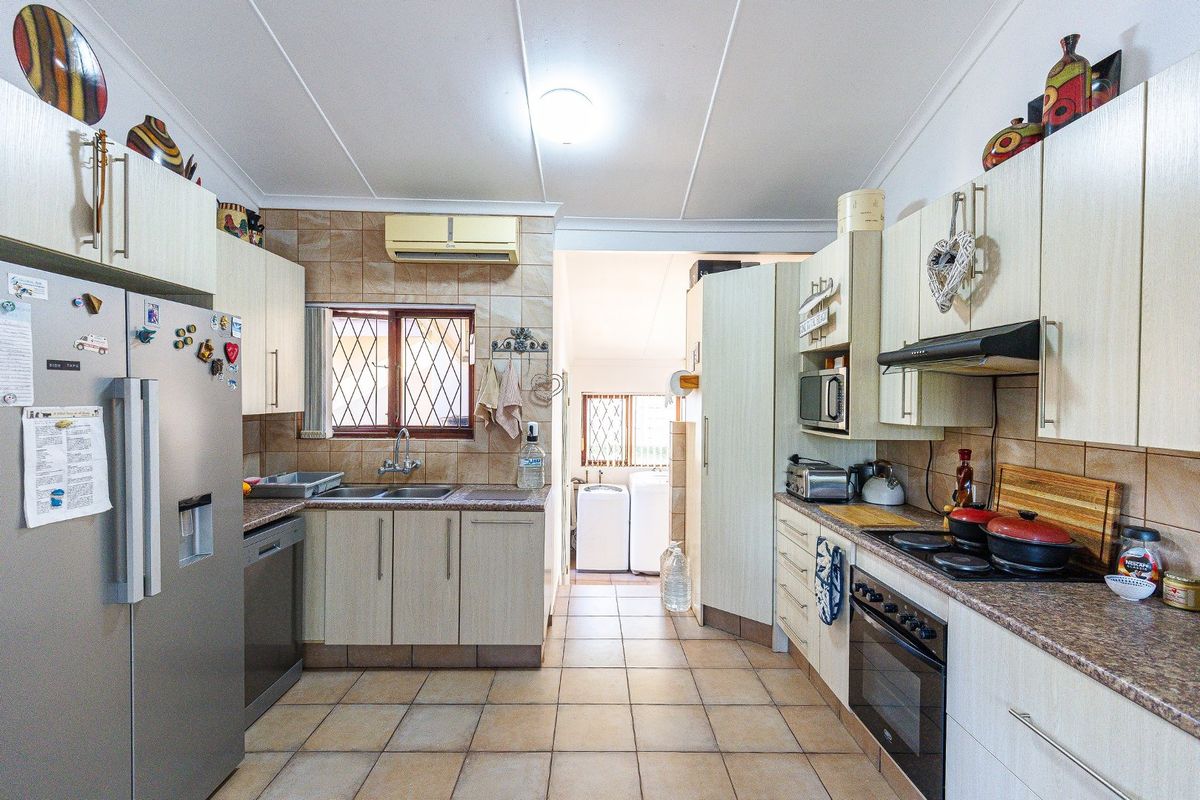 Functional kitchen featuring light-toned cabinetry, tiled splashbacks, built-in oven, hob, extractor fan, and double sink, with an adjacent laundry area visible.